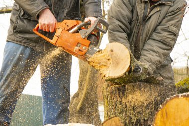 Mavi pantolonlu bir adam elektrikli testereyle tahta testeresi kesiyor.