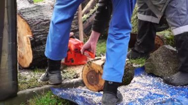 Mavi takım elbiseli adamlar elektrikli testereyle odun kesiyorlar.