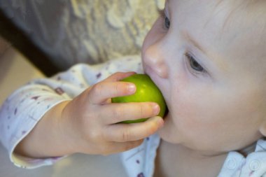 Sarı saçlı, elinde yeşil domates olan küçük bir kız.