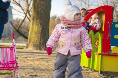Pembe ceketli küçük bir kız çocuk parkında oturuyor.