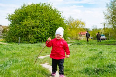Kırmızı ceketli küçük bir kız yeşil çimlerde yürüyor.
