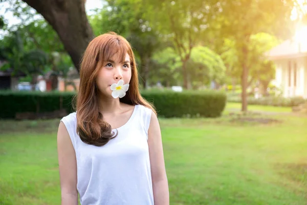 Retrato de linda chica asiática siendo el uso de la boca morder una flor de plomería y sol en el parque, relajarse tiempo, verano, disfrutar y feliz . — Foto de Stock