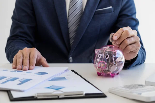 Empresario poniendo monedas en alcancía y utilizando la calculadora t — Foto de Stock