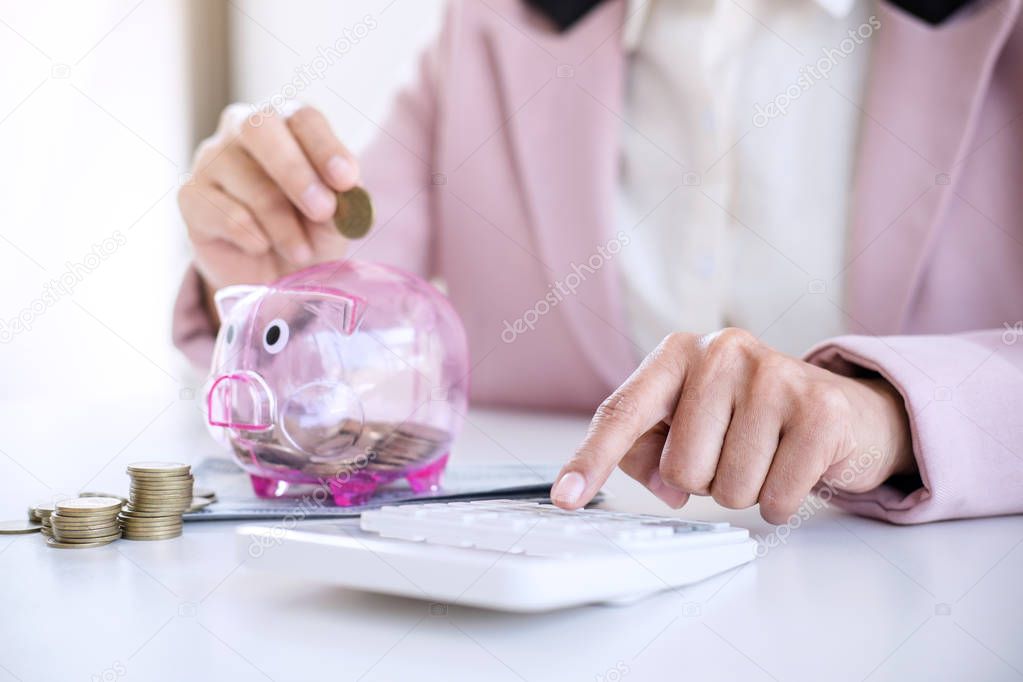 Business woman putting coins into piggy bank and using calculato