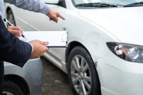保险代理人检查损坏的汽车和归档报告索赔表格 — 图库照片