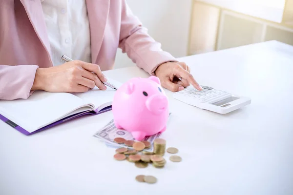 Business woman putting coins into piggy bank, writing to report