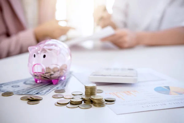 Two couples putting coins into piggy bank, writing to report and — Stock Photo, Image
