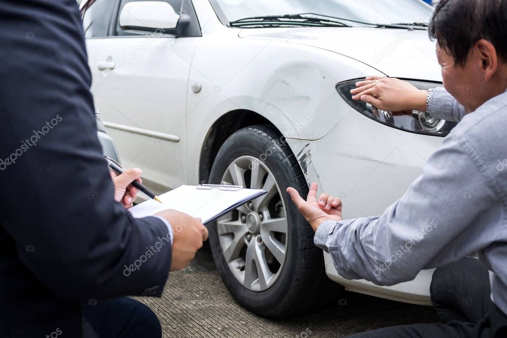 Man agent Filling Insurance Form Near Damaged and examining Car,