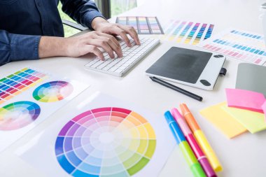 İş yerinde iş araçları ve aksesuarlarıyla renk seçimi ve grafik tableti üzerinde çalışan erkek yaratıcı grafik tasarımcı resmi.