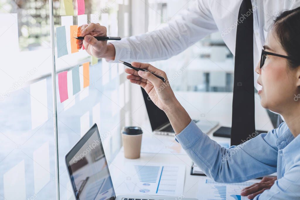 Teamwork of business team consulting market growth on financial document graph report statistics, using post it notes in glass wall to writing strategy business plan to development grow to success.