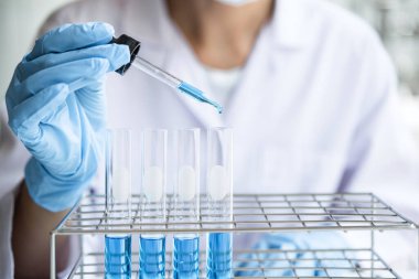 Laboratuvarda çalışan cam teçhizatı üzerine bir damla renk sıvısı ile mikroskop reaktörü kullanarak laboratuvar önlüğü içinde bilim adamı ya da tıbbi araştırma..