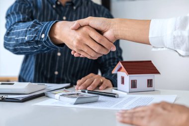 Emlakçı ve müşteriler el sıkışıyor. Ev sigortası, yatırım kredisi, tokalaşma ve başarılı bir anlaşma imzalandıktan sonra bitirilen sözleşmeyi kutluyorlar..