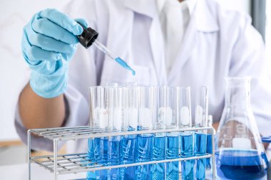 Biyokimya laboratuvarı araştırması, laboratuvar önlüğündeki tıp veya bilim adamı laboratuarda çalışan cam teçhizatların üzerine bir damla renk sıvısı içeren test tüpü kullanıyor..