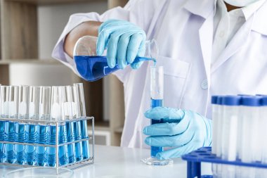 Biyokimya laboratuvarı araştırması, laboratuvar önlüğündeki tıp veya bilim adamı laboratuarda çalışan cam teçhizatların üzerine bir damla renk sıvısı içeren test tüpü kullanıyor..