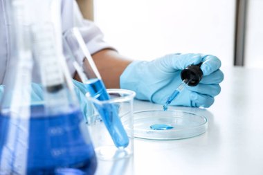 Biyokimya laboratuvarı araştırması, laboratuvar önlüğündeki tıp veya bilim adamı laboratuarda çalışan cam teçhizatların üzerine bir damla renk sıvısı içeren test tüpü kullanıyor..
