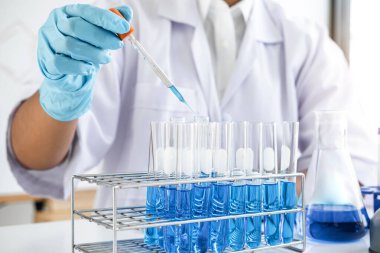 Biyokimya laboratuvarı araştırması, laboratuvar önlüğündeki tıp veya bilim adamı laboratuarda çalışan cam teçhizatların üzerine bir damla renk sıvısı içeren test tüpü kullanıyor..