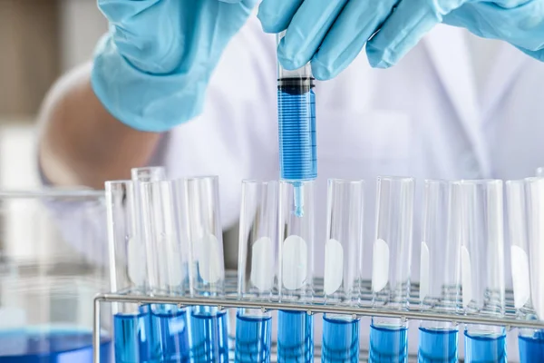 Biyokimya laboratuvarı araştırması, laboratuvar önlüğündeki tıp veya bilim adamı laboratuarda çalışan cam teçhizatların üzerine bir damla renk sıvısı içeren test tüpü kullanıyor..