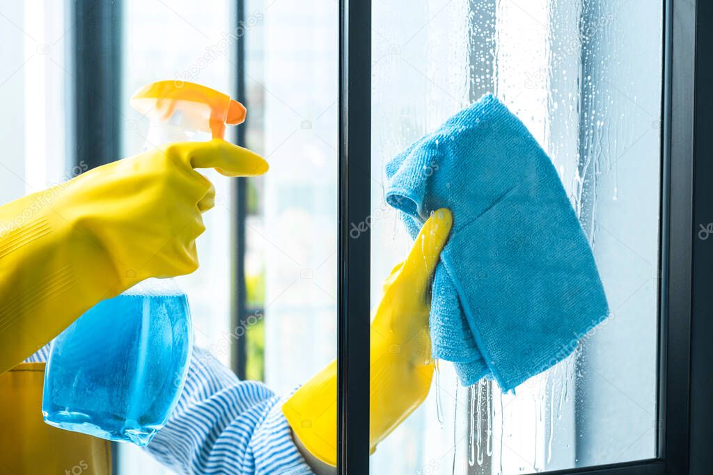 Wife housekeeping and cleaning concept, Happy young woman wiping dust using a spray and a duster while cleaning in glass at home.