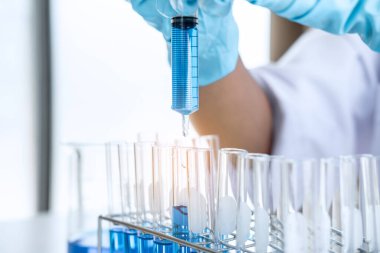 Biyokimya laboratuvarı araştırması, laboratuvar önlüğündeki tıp veya bilim adamı laboratuarda çalışan cam teçhizatların üzerine bir damla renk sıvısı içeren test tüpü kullanıyor..