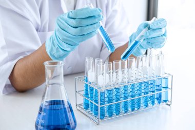Biyokimya laboratuvarı araştırması, laboratuvar önlüğündeki tıp veya bilim adamı laboratuarda çalışan cam teçhizatların üzerine bir damla renk sıvısı içeren test tüpü kullanıyor..