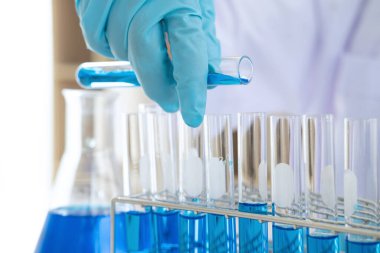 Biyokimya laboratuvarı araştırması, laboratuvar önlüğündeki tıp veya bilim adamı laboratuarda çalışan cam teçhizatların üzerine bir damla renk sıvısı içeren test tüpü kullanıyor..