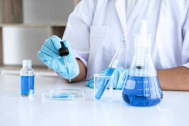 Biyokimya laboratuvarı araştırması, laboratuvar önlüğündeki tıp veya bilim adamı laboratuarda çalışan cam teçhizatların üzerine bir damla renk sıvısı içeren test tüpü kullanıyor..