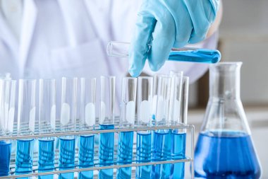 Biyokimya laboratuvarı araştırması, laboratuvar önlüğündeki tıp veya bilim adamı laboratuarda çalışan cam teçhizatların üzerine bir damla renk sıvısı içeren test tüpü kullanıyor..