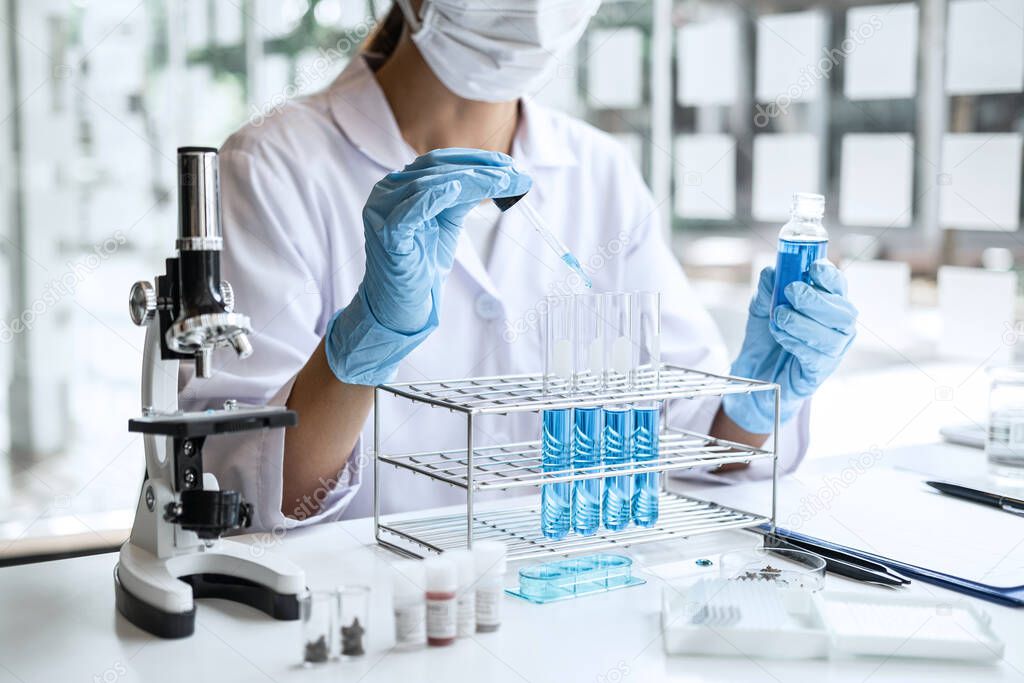 Biochemistry laboratory research, Scientist or medical in lab coat holding test tube with Using Microscope reagent with drop of color liquid over glass equipment working at the laboratory.