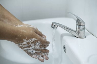 Banyoda, banyo musluğunun altında ellerini yıkayan kadın temizlik ve önleme için sabun jeli kullanıyor..