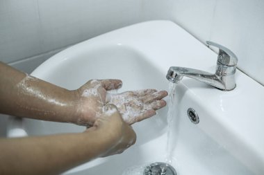 Banyoda, banyo musluğunun altında ellerini yıkayan kadın temizlik ve önleme için sabun jeli kullanıyor..