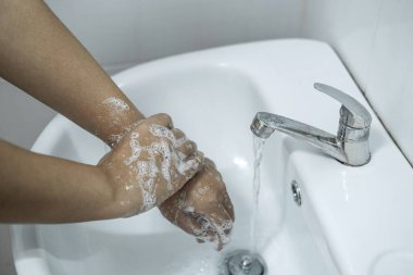Banyoda, banyo musluğunun altında ellerini yıkayan kadın temizlik ve önleme için sabun jeli kullanıyor..