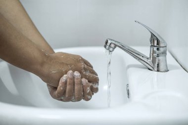 Banyoda, banyo musluğunun altında ellerini yıkayan kadın temizlik ve önleme için sabun jeli kullanıyor..