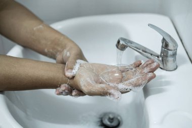 Banyoda, banyo musluğunun altında ellerini yıkayan kadın temizlik ve önleme için sabun jeli kullanıyor..