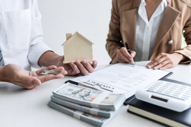 Emlakçı Satış Müdürü, kira kontratı ve konut sigortası için ipotek kredisi teklifiyle ilgili satış sözleşmesini imzaladıktan sonra müşterinin dosyalama anahtarlarını tutuyor..