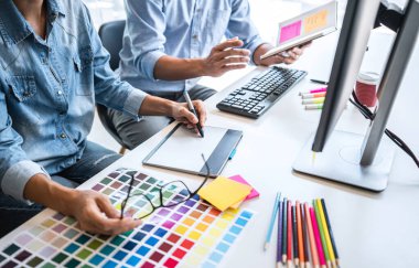 Renk seçimi ve renk örnekleri üzerinde çalışan iki iş arkadaşı yaratıcı grafik tasarımcısı, çalışma araçları ve aksesuarlarla iş yerindeki grafik tabletine çizim yapıyor.