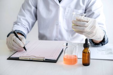 Laboratuvar önlüğündeki bilim adamı ya da tıp laboratuvar önlüğündeki deney tüpünü reaktörle tutarak cam şişede reaksiyonları karıştırarak kimyasal sıvı, laboratuvar araştırmaları ve testler içeren cam kaplar oluşturuyorlar..