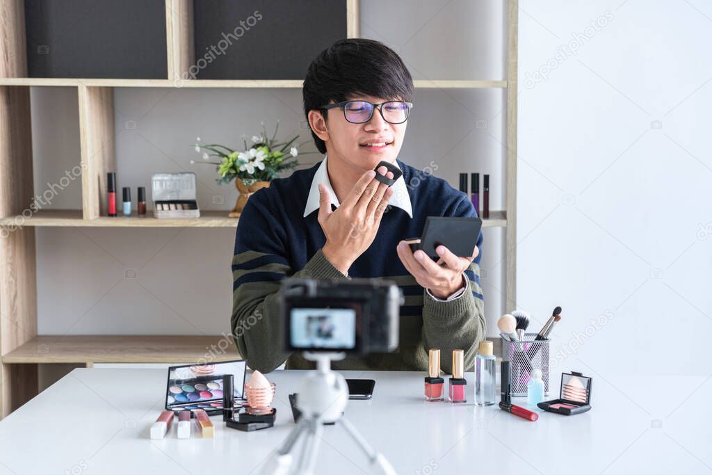 Happy smiling elegant man blogger is showing present make up tutorial beauty cosmetic review product and broadcast live streaming video blogging to social network teaching online on camera screen.