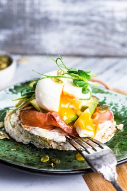 Kızarmış yumurtalı tost, füme somon, avokado, ızgara domates ve bebek ıspanağı. Mikroyeşil. Sağlıklı gıda konsepti. Çıtır ekmek, ekmek kırıntıları. Diyet gıda konsepti