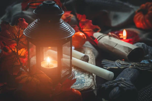 Close-up glowing lantern and different medieval or a fairy tale objects such as candles, a rolled letter, a sword and a book on textile background. Cozy autumn background