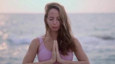 Hamile kadın yoga yapıyor, vrksasana pozisyonunda duruyor sahilde, kayalıklarda. Meditasyon yapan bir kızın elleri. Kızın elleri karnının üstünde. Güneşi selamlayın. Pembe eşofmanlı Hatha yoga kadını. Dövmeli kadın. Sakin ol.