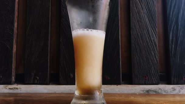 ガラスの泡と滴下凝縮液で冷たい光ビールビールビールマグカップに注ぐビールのスローモーションショット 白ビール泡はマグカップの縁を超えています 黒の背景の上のガラス ストック映像