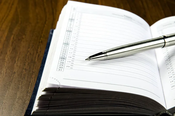 Vista de cerca de una pluma de metal que se encuentra en el diario con un calendario —  Fotos de Stock