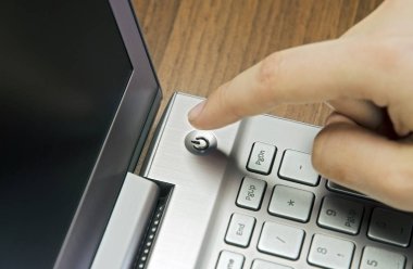 Bir el ile bir parmak portre görünümünü Metalik Gümüş dizüstü klavye üzerinde ahşap mat bulanık yalan, güç düğmesine basın