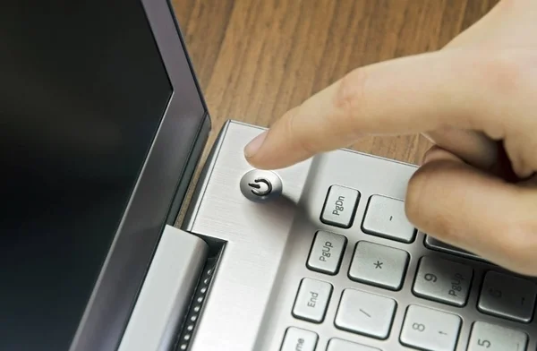 Крупный план руки пальцем, нажмите кнопку питания на металлической серебряной клавиатуре ноутбука, лежащей на деревянном коврике размытие — стоковое фото