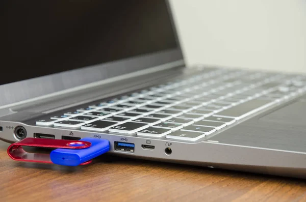 Vista close-up de um laptop prateado com disco flash azul anexado em uma mesa de madeira e em um fundo branco — Fotografia de Stock