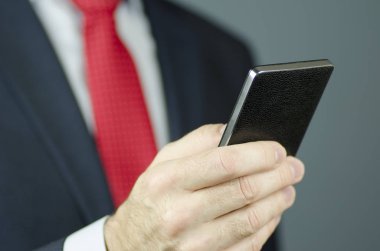 Bir yöneticinin el ile bir takım elbise ve siyah bir smartphone kullanarak kırmızı kravat ile yakından görmek