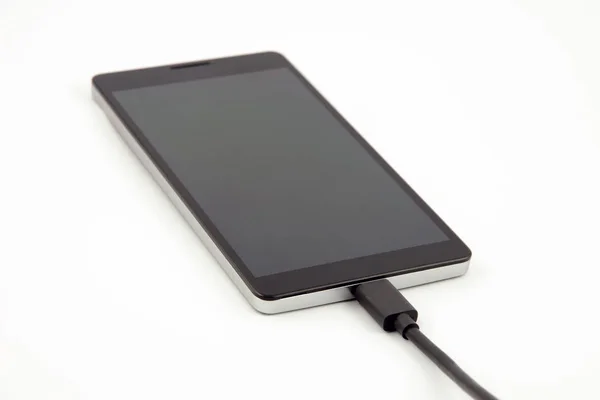 Вид крупным планом мобильного телефона - смартфона - с прикрепленным черным кабелем зарядки на белом фоне — стоковое фото