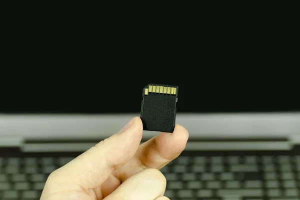 Vista de perto de uma mão segurando um cartão de memória SD preto com um laptop de fundo, isolado em segundo plano — Fotografia de Stock