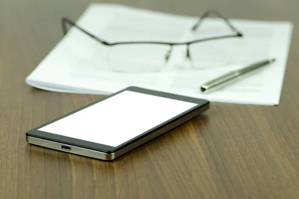 Uma visão detalhada de uma mesa de negócios com um telefone celular com uma tela branca em branco, caneta com papel e óculos com um fundo embaçado — Fotografia de Stock