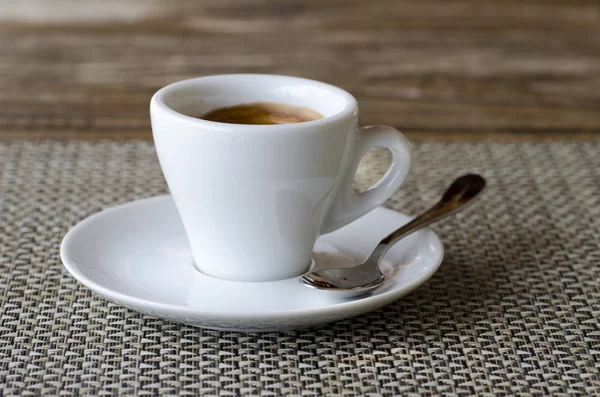 Foto de primer plano de café expreso en taza de porcelana blanca en platillo con cuchara de pie sobre la mesa —  Fotos de Stock